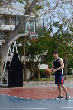 Genç bir erkek atlet halka açık bir sahada basketbol oynuyor. Spor, enerji ve sağlıklı yaşam tarzı konsepti.