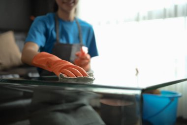 Lastik eldivenlerle temizlik işçisi modern evde cam masayı bezle siliyor..