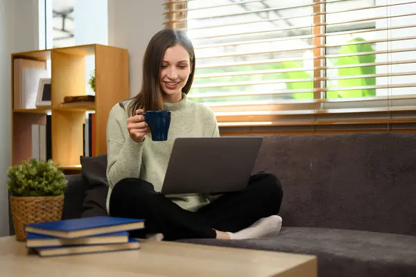 美丽的高加索女人在家里客厅里喝茶和使用笔记本电脑 — 图库照片