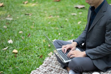 Resmi takım elbiseli vurulan iş adamı yeşil çimlerde dizüstü bilgisayarla çalışıyor..