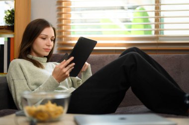 Oturma odasındaki kanepede dijital tablet kullanan güzel bir kadın..