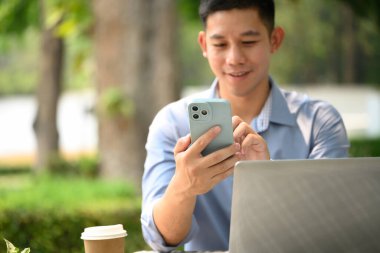 Gülümseyen genç işadamı kafenin önünde cep telefonundan mesaj atıyor..
