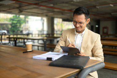 Gülümseyen işadamı kafeteryada oturuyor ve dijital tabletindeki e-postaları kontrol ediyor..