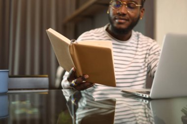 Yemek odasındaki masada dizüstü bilgisayar kullanan Afro-Amerikalı bir adam..