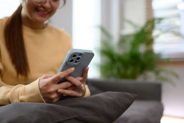 Evdeki kanepede oturan ve cep telefonuna mesaj yazan genç bir kadının kırpılmış görüntüsü..