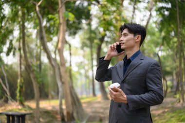 Şehir parkında dururken cep telefonuyla konuşan yakışıklı genç işadamı..