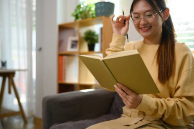 Evde kulaklıkla müzik dinleyen ve kitap okuyan güzel genç bir kadın..