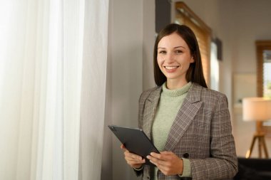 Bin yıllık iş kadını portresi dijital tablet tutuyor ve kameraya güvenle gülümsüyor..