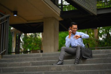 Mutlu iş adamı cep telefonuyla konuşuyor ve dışarıdaki kol saatini kontrol ediyor..