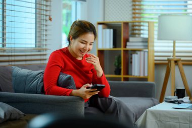 Kanepede dinlenen ve cep telefonunda mesaj okuyan güzel bir genç kadın..