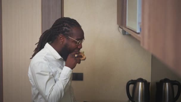 キッチンに立っている間 おいしいバーガーを噛む若いアフリカ人男性 スローモーションショット — ストック動画