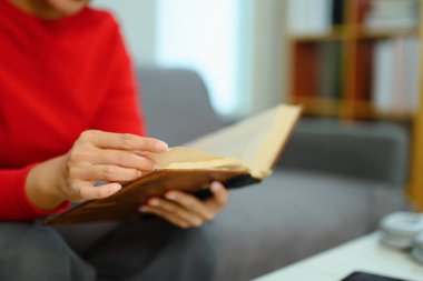 Sıcak süveter giyen, evdeki kanepede kitap okuyan genç bir kadın..