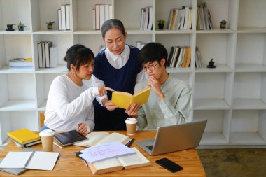 Sınıfta grup projesinde çalışan öğrencilerine yardım eden gülümseyen bayan öğretim görevlisi..