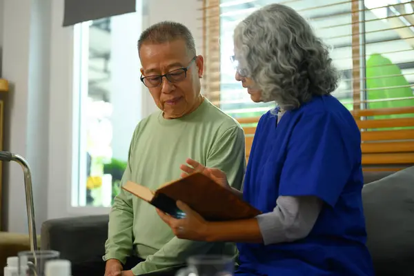 看護師の看護師は 老人ホームでソファーの上の高齢者に本を読んでいる ボランティア ホームヘルスケアサービスコンセプト ロイヤリティフリーのストック画像