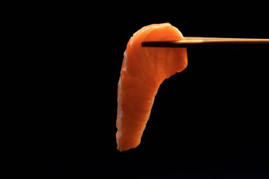 Siyah arka planda taze somon balığı ile yakın plan yemek çubukları..