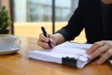 Siyah takım elbiseli vurulan muhasebeci ahşap masada mali raporlarla çalışıyor..