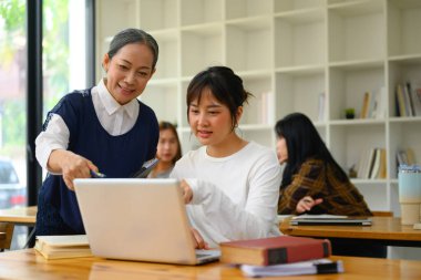 Gülümseyen kıdemli profesör ders sırasında öğrencilere dizüstü bilgisayarda yardım ediyor..