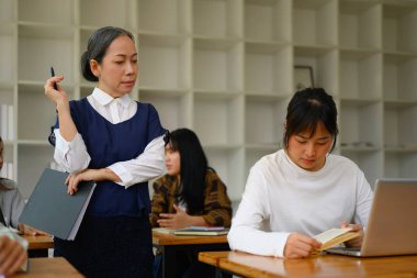 Yetişkin bir profesörün sınıfta yürümesi ve öğrenci ödevlerini kontrol etmesi..
