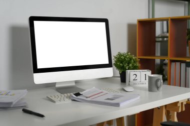 Finansal raporları ve kahve fincanı olan beyaz masadaki boş ekran bilgisayar.
