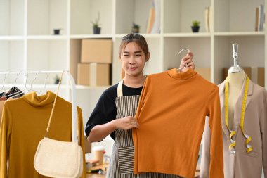 Güzel, genç bir bayan. Küçük bir işletme sahibi elbise mağazasında askılık tutuyor..