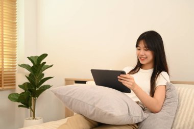 Evde uzaktan çalışırken dijital tablet kullanarak gülümseyen serbest çalışan kadın..