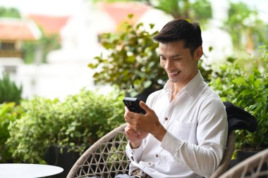 Kafe terasında cep telefonu kullanan gülümseyen işadamı.