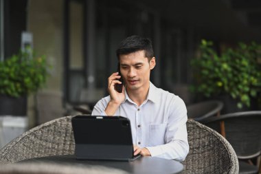 Asyalı işadamı telefon görüşmesi yapıyor ve modern kafenin terasında dijital tablet kullanıyor..