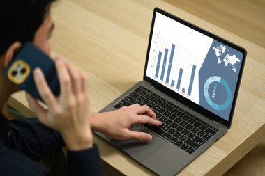 Kırpılmış erkek serbest çalışan cep telefonuyla konuşuyor ve evde dizüstü bilgisayar kullanıyor..