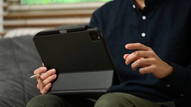 Evdeki kanepede oturup dijital tablet kullanan genç işadamını kapat..