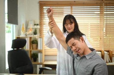 Kadın fizyoterapist, modern klinikte omzu ağrıyan hastayı muayene ediyor..