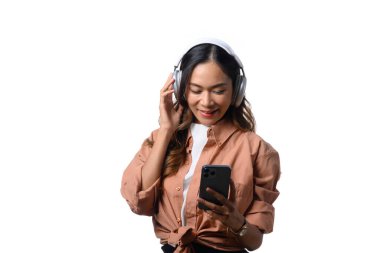 Beyaz arka planda izole edilmiş cep telefonu kullanarak kulaklıkla müzik dinleyen çekici genç bir kadın..