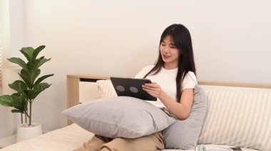 Evde uzaktan çalışırken dijital tablet kullanarak gülümseyen Asyalı serbest çalışan kadın..