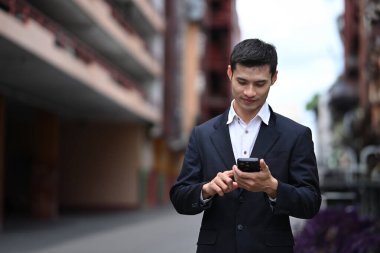 Gülümseyen Asyalı işadamı şehir sokağında dururken cep telefonu kullanıyor..
