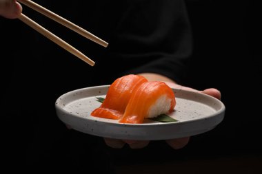 Elinde somonlu Nigiri suşisi ve siyah arka planda çubuk tutan adam. Japon yemek tarzı konsept.