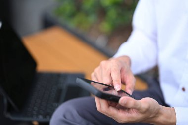 İş adamı ofis binasının önünde otururken cep telefonuna mesaj yazıyor.