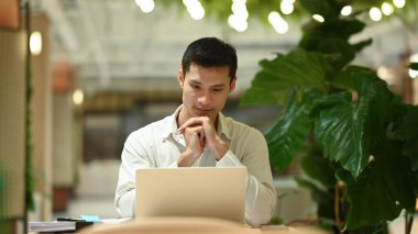 Modern bir çalışma alanında oturan çekici iş adamı dizüstü bilgisayar kullanıyor..