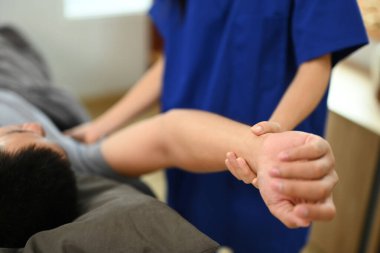 Bir rehabilitasyon kliniğinde erkek hasta dondurulmuş omuz semptomlarını inceleyen yakın doktor..