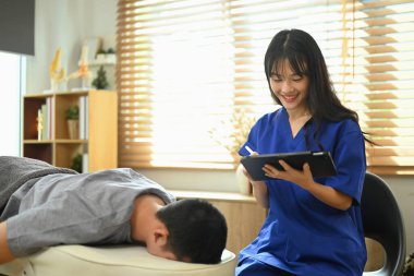 Klinikte erkek hastayı muayene ederken dijital tablet kullanan gülümseyen kadın fizyoterapist..