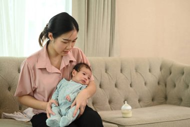 Mutlu, gülümseyen bir anne ve evde kanepede oturan küçük, tatlı bir erkek bebek. Annelik ve çocuk bakımı kavramı.