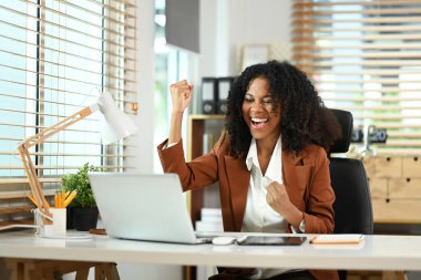 Heyecanlı afro-amerikan iş kadını evet diyerek, başarısını kutlarken dizüstü bilgisayarında iyi haberler okuyor..
