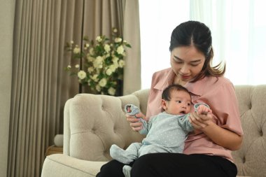 Mutlu, gülümseyen bir anne ve evde kanepede oturan küçük, tatlı bir erkek bebek. Annelik ve çocuk bakımı kavramı.