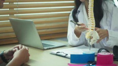Fizyoterapist, muayene odasında erkek hastayı omurilik modeliyle eğitiyor..