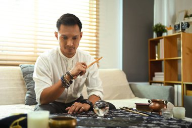 Erkek tarot okuyucu çeşitli manevi öğelerle çevrili masada tahminlerde bulunuyor.