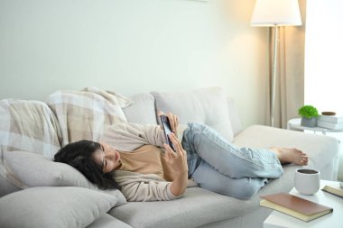 Oturma odasındaki koltukta cep telefonu kullanan güzel bir Asyalı kadın..