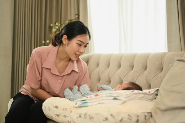 Şefkatli genç anne, açık mavi tulumuyla uyuyan bebeğine şefkatle bakıyor. Annelik ve çocuk bakımı kavramı.