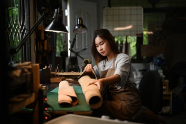 Atölyesinde deri kumaş üzerinde çalışan önlük giyen gülümseyen bir zanaatkarın portresi..