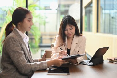 Dijital tablet kullanan ve ortak çalışma alanında finansal verileri analiz eden gülümseyen Asyalı kadın meslektaşlar.