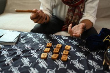 Falcı, mistik bir bezle kaplı bir masanın üzerine tahta mühürler diziyor. Tahmin ve kehanet kavramı.