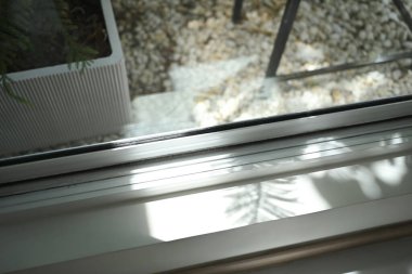 Pencere çerçevesi güneş ışığının aktığı, yakındaki bitkilerin gölgelerini oluşturan. Ev, sükunet ve doğa kavramıyla bağlantı.