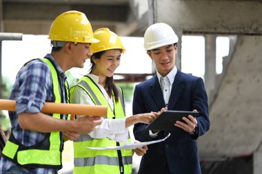 Dijital tablet kullanan ve inşaat alanındaki projeyi tartışan inşaat profesyonelleri..